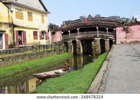 HOI AN, VIETNAM - FEB 3 - 2015 - Old man paddles his boat in a canal with Japnese Covered Bridge in the background,  Hoi An, Vietnam