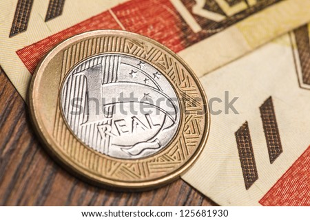 One Brazilian Real coin, over a 20 Real bill. Studio Shot.