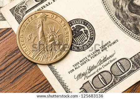 One Dollar coin, over a 100 Dollar bill. Studio Shot.