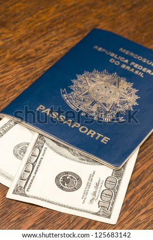 Brazilian Passport with Dollar bills over a wooden table.