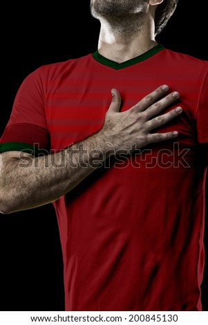 Portuguese soccer player, listening to the national anthem with his hand on his chest. On a black background.