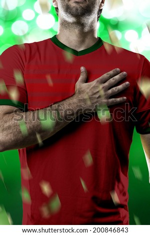 Portuguese soccer player, listening to the national anthem with his hand on his chest. On a green lights background.