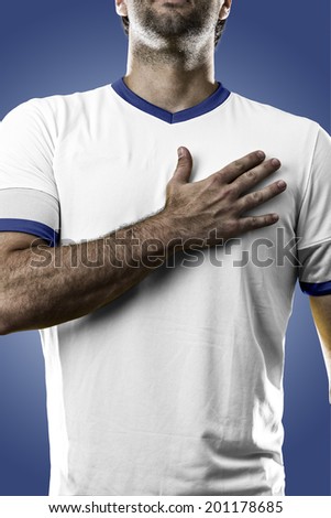 Greek soccer player, listening to the national anthem with his hand on his chest. On a blue background.