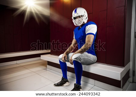 Football Player with a blue uniform seated in locker room.