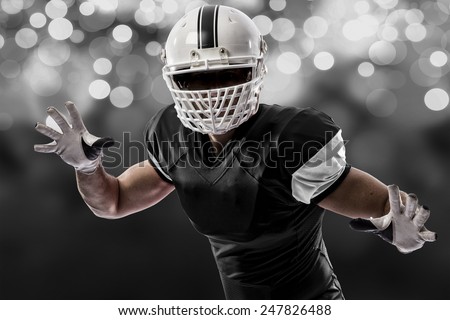Football Player with a black uniform making a tackle on a black lights background.