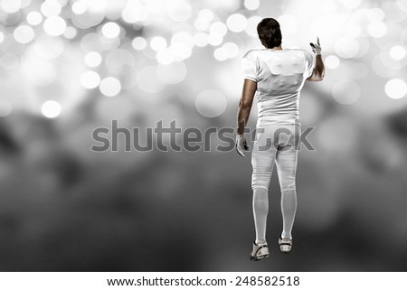 Football Player with a white uniform walking, showing his back on a white lights background.