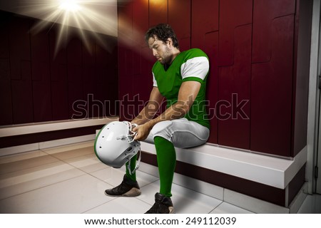 Football Player with a green uniform seated in locker room.