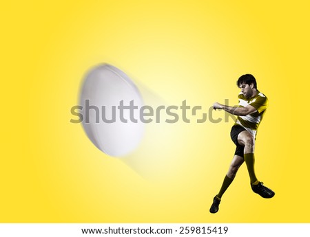 Rugby player in a yellow uniform kicking a ball on a yellow background.