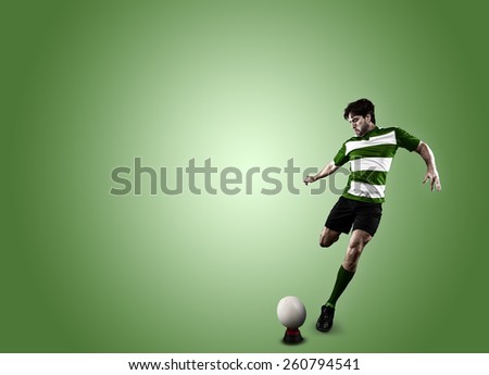 Rugby player in a green uniform kicking a ball on a green backgrond.