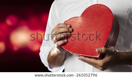 A Man holding a heart gift box in a gesture of giving in a red lights background