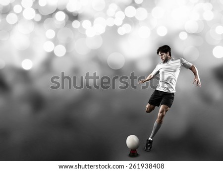 Rugby player in a white uniform kicking a ball on a white lights background.