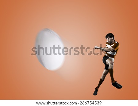 Rugby player in a orange uniform kicking a ball on a orange background.