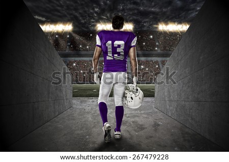 Football Player with a purple uniform walking out of a Stadium tunnel.
