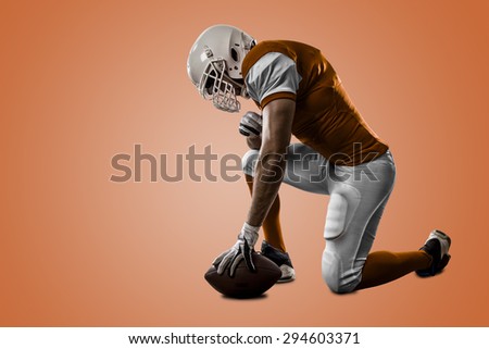Football Player with a orange uniform on his knees, on a orange background.