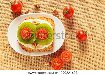 Toast with kiwi, cheese and cherry tomato  on a piece of sackcloth with walnuts and cherry tomatoes around. View from above