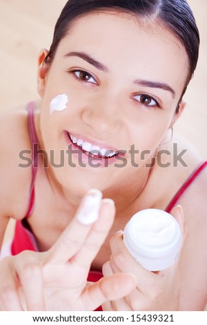 young smiling woman applying cream on her face