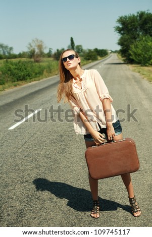Attractive young woman hitchhiking along a road.