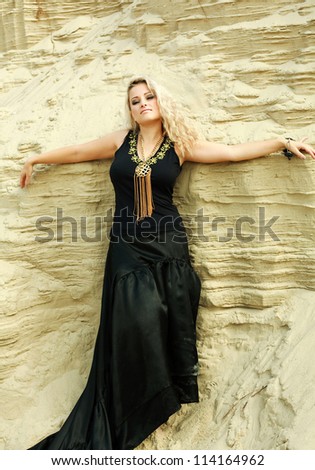 Fashion blond girl in long black dress posing in sand desert with closed eyes