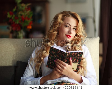 Happy young woman reading book on couch at home