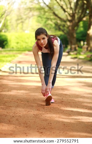 Sportive girl exercising outdoor in summer park before a run, training outdoors