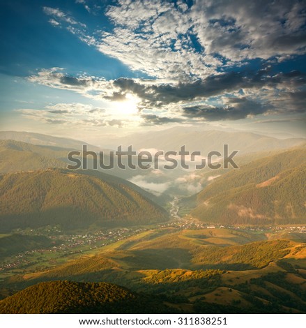 Valley in mountains at dawn, lighted by the sun, on a sky background