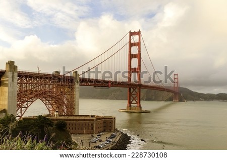 The famous San Francisco Golden Gate Bridge in California, United States of America. A view of Fort Point, the bay, surfers and the red suspended bridge connecting Frisco to Marin County at sunset.
