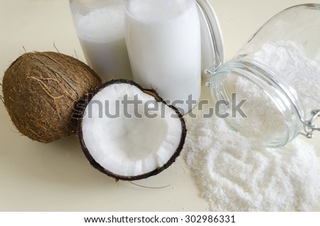 Coconut products. Cracked open coconut with meat cut in half, grounded flakes in a mason jar, flour and fresh milk in glass bottles on a table with a heart shaped shot from the top