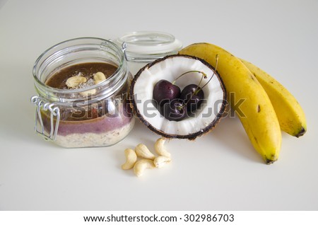 Cherry coconut banana overnight oats with cracked open coco, banana, cashews mixed with chia seeds and cherry cream in a mason jar,a tropical meal on white background.Healthy fitness breakfast oatmeal