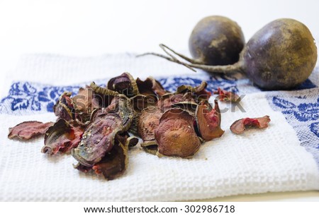 Thin round beetroot chips baked in the oven with oregano and salt and ripe beet roots in the white background. A healthy, vegetarian, vegan, crispy snack appetiser for diet and clean eating.