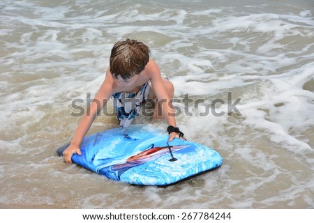 young caucasian boy in surf with blue boogie board