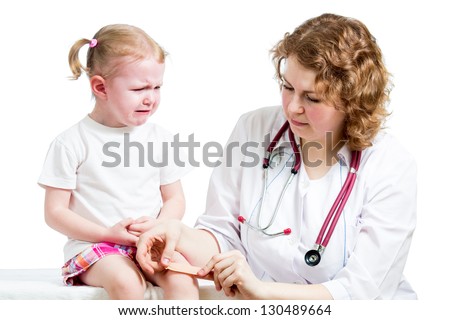 Crying child with scratched knee. Doctor provides first aid.