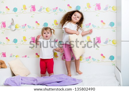 children sisters play and jump on the bed