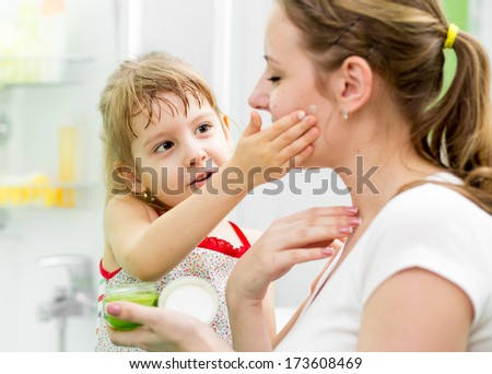 kid daughter putting cream on her mother\'s face in bathroom