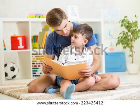 kid boy and his father read a book on floor at home