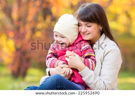 happy young mother and her daughter have fun sitting at autumn background