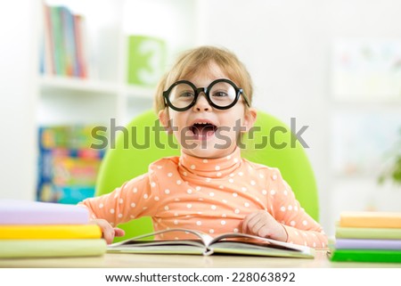 Happy funny kid girl in glasses reading a book in primary school