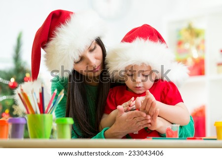 child girl and mom in Santa hats making christmas tree of plasticine