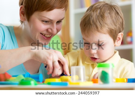 smiling woman and  child boy play colorful clay toy at playschool or home