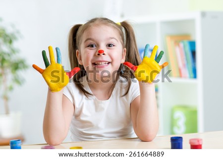 cute cheerful girl showing her painted hands in playroom