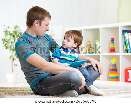 dad and son kid playing with tablet computer indoors