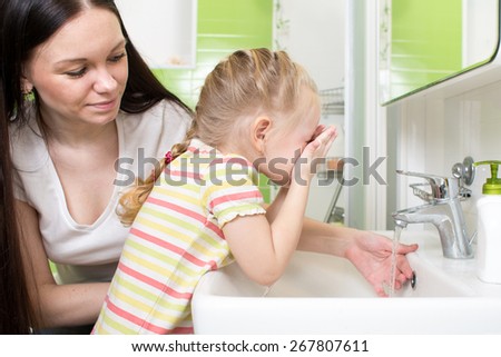 Cute little girl with mom washing face in bathroom
