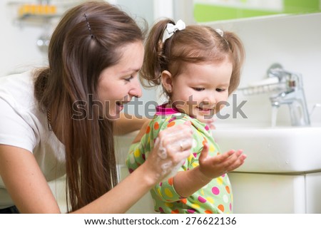 Smiling girl child and her mother washing hands and face with soap in the bathroom. Hygiene.