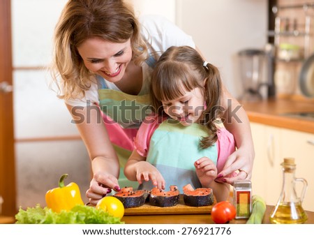 Cute mother with child daughter preparing fish in kitchen
