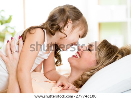 Happy middle-aged mom playing with her kid daughter in bed enjoying  sunny morning in home bedroom