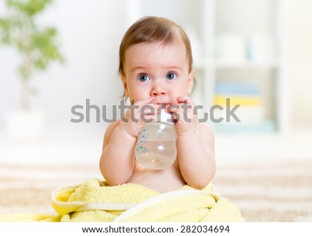 baby drinks water from bottle sitting with towel at home