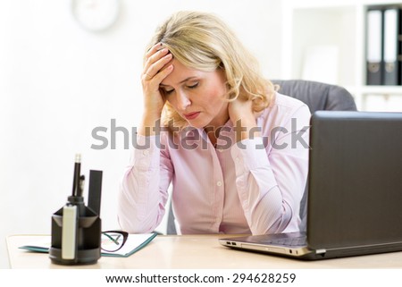 Tired middle-aged business woman in her office looking down