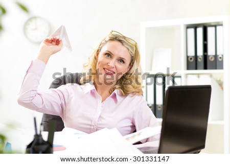 Middle-aged business woman throwing paper airplane in office