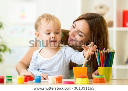 cute kid boy painting with paintbrush at home or day care center