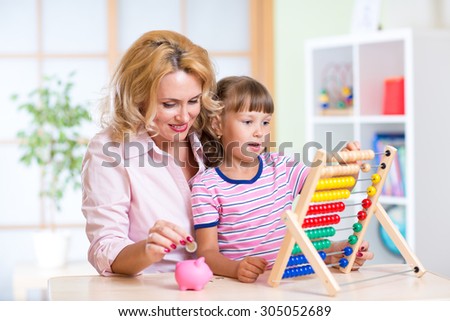 Mother and kid daughter putting coins into piggy bank. Child plays with abacus.