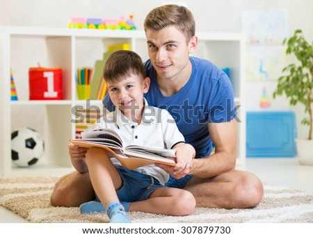 cute smiling kid and his dad read a book in children room